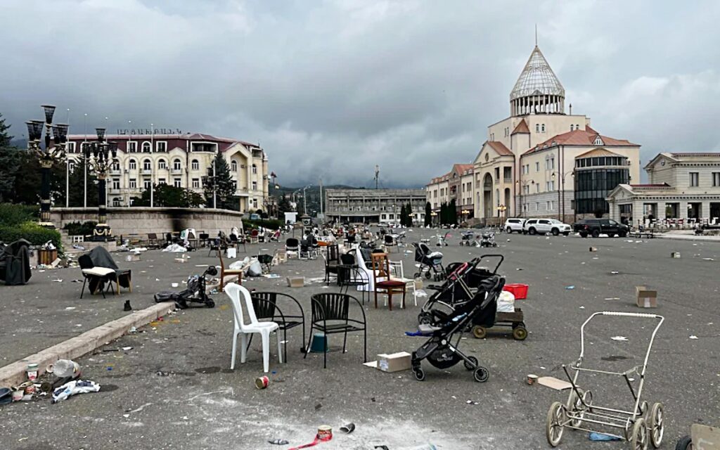 A haunting scene in the central square of Stepanakert, the capital of Artsakh (Nagorno-Karabakh), showing abandoned strollers, chairs, and scattered belongings. The desolation reflects the forced displacement of over 120,000 Armenians following Azerbaijan’s 2023 military assault and ethnic cleansing of the region.