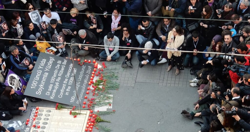 Ani Boghikian-Kasparian at the 2015 Armenian Genocide commemoration in Istanbul’s Beyoğlu, seated with hundreds around candles and posters honoring arrested Armenian intellectuals.