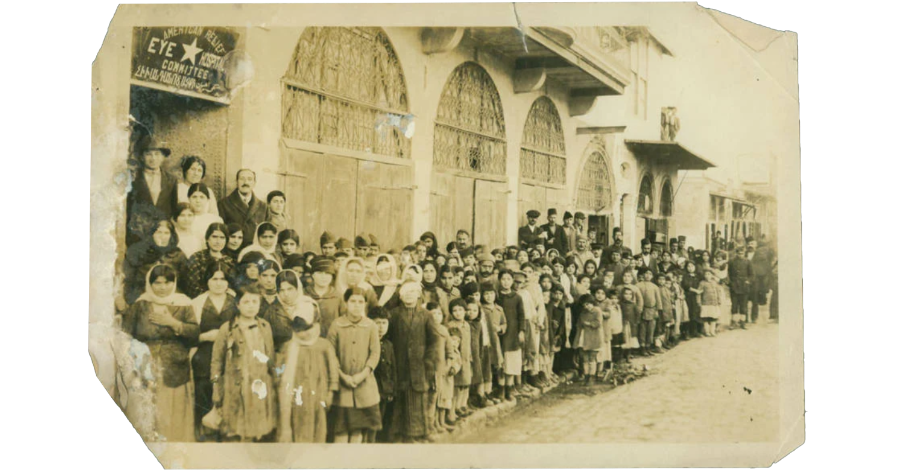 A large group of Armenian Genocide survivors, including women and children, standing outside the American Relief Eye Committee building, circa 1920s, showing the scale of humanitarian aid after The Genocide.