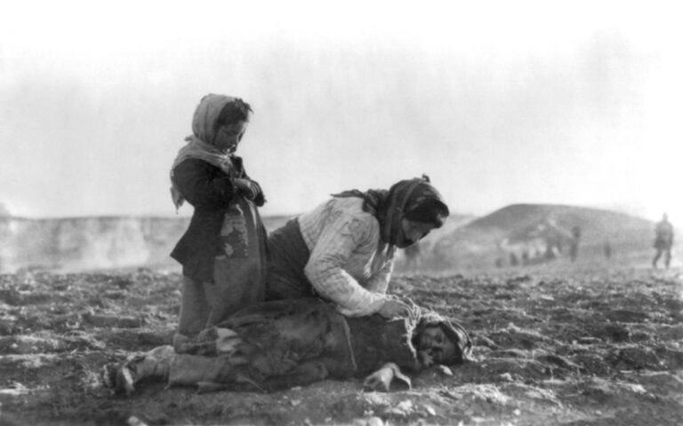 Armenian mother kneeling over her dead child on the desert ground during the genocide death marches, with another child standing beside her.